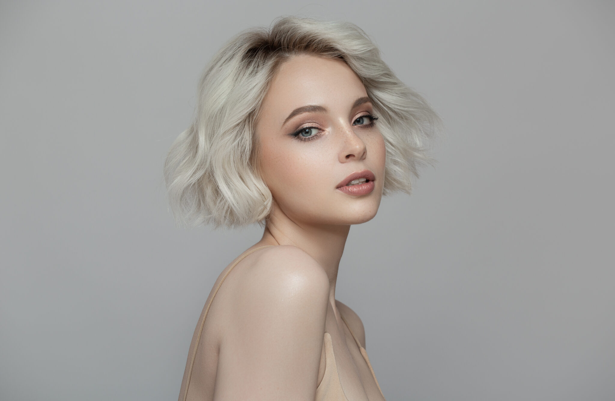 Blonde girl with short haircut against gray background, conveying youthful vitality.